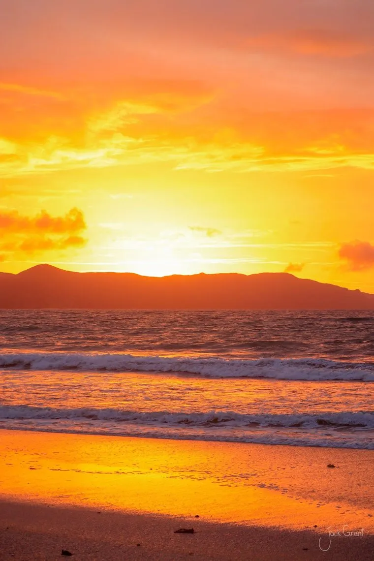 Sunset over the sea at Spirits Bay, orange light reflected on wet sand, Far North, New Zealand